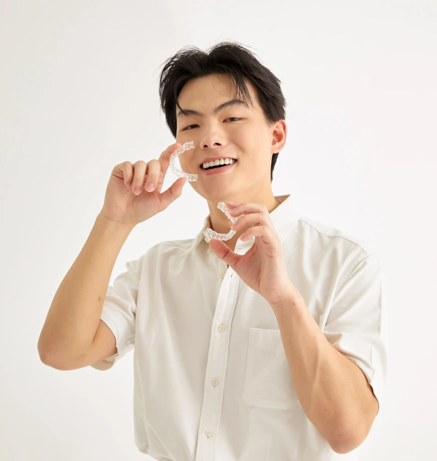 Man smiling while holding clear aligners in both hands